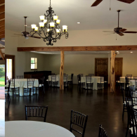 Empty banquet hall with chandeliers, ceiling fans, and tables and chairs arranged around the room