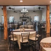 Elegant banquet hall with round tables, black chairs, chandeliers, and a fireplace at the far end