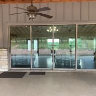 Covered patio with sliding glass doors, ceiling fan, and brick flooring overlooking a grassy yard
