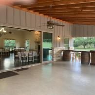 Open-air patio with polished concrete floor, wooden ceiling, and bar stools beside glass doors.
