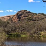 Rocky hillside above a small pond with sparse trees under a blue sky