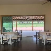 Open-air dining area with white tablecloth tables overlooking a grassy field