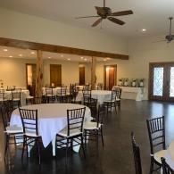 Empty banquet hall with round tables, black chairs, and ceiling fans under warm lighting