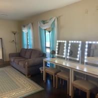 Living room with gray sofa, patterned rug, vanity table with lit mirrors, and blue curtains on the windows