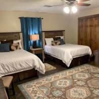 Bedroom with two beds, patterned rug, blue curtains, ceiling fan, and wooden closet doors