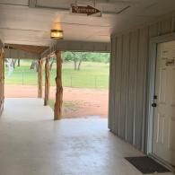Covered porch with hanging light and a white door, overlooking a grassy yard and dirt path.
