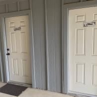 Two white apartment doors with black doormats in a gray hallway