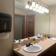 Bathroom vanity with mirror, sink, soap dispenser, and overhead lights in a beige interior