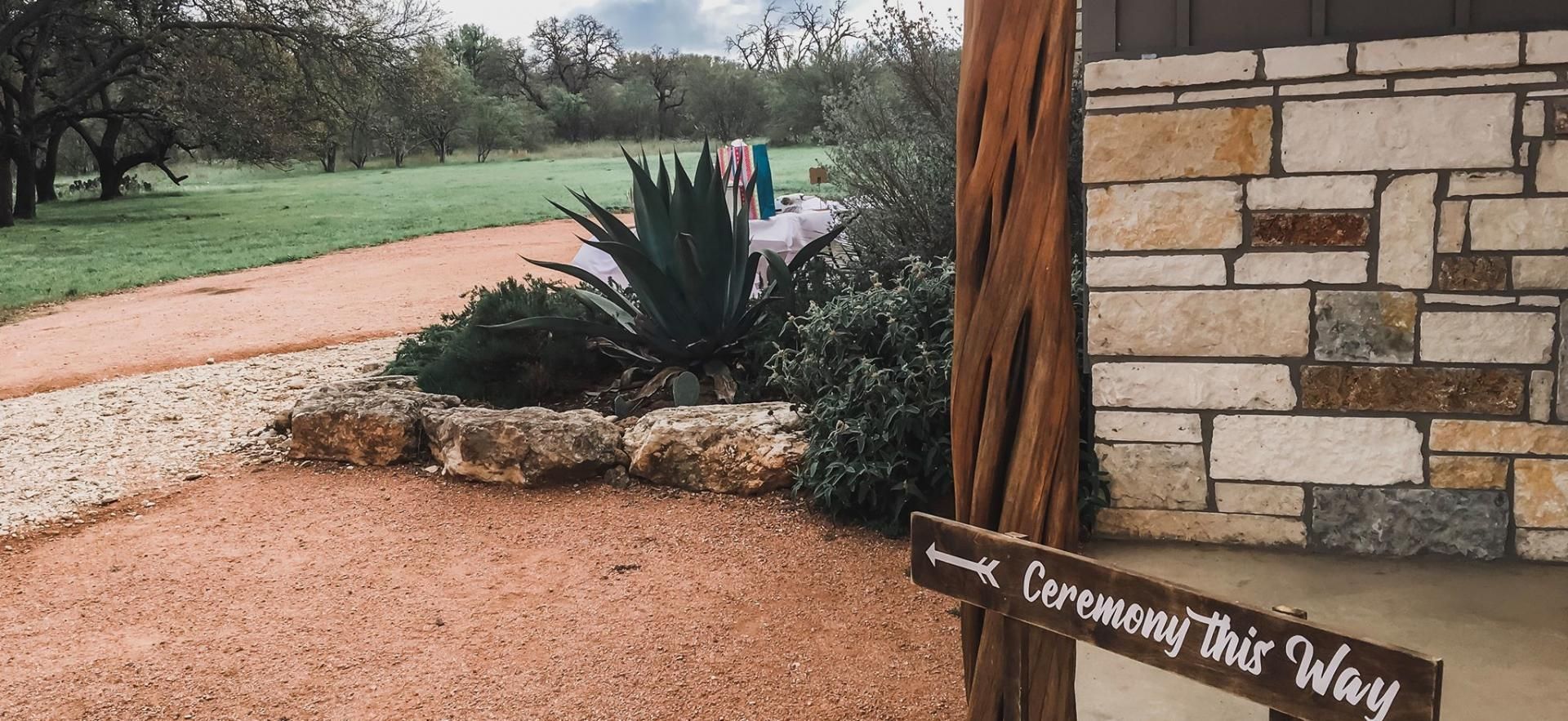 Ranch-style entry with gravel path, stone wall, agave, and sign reading “Walk by Faith, Not by Sight”