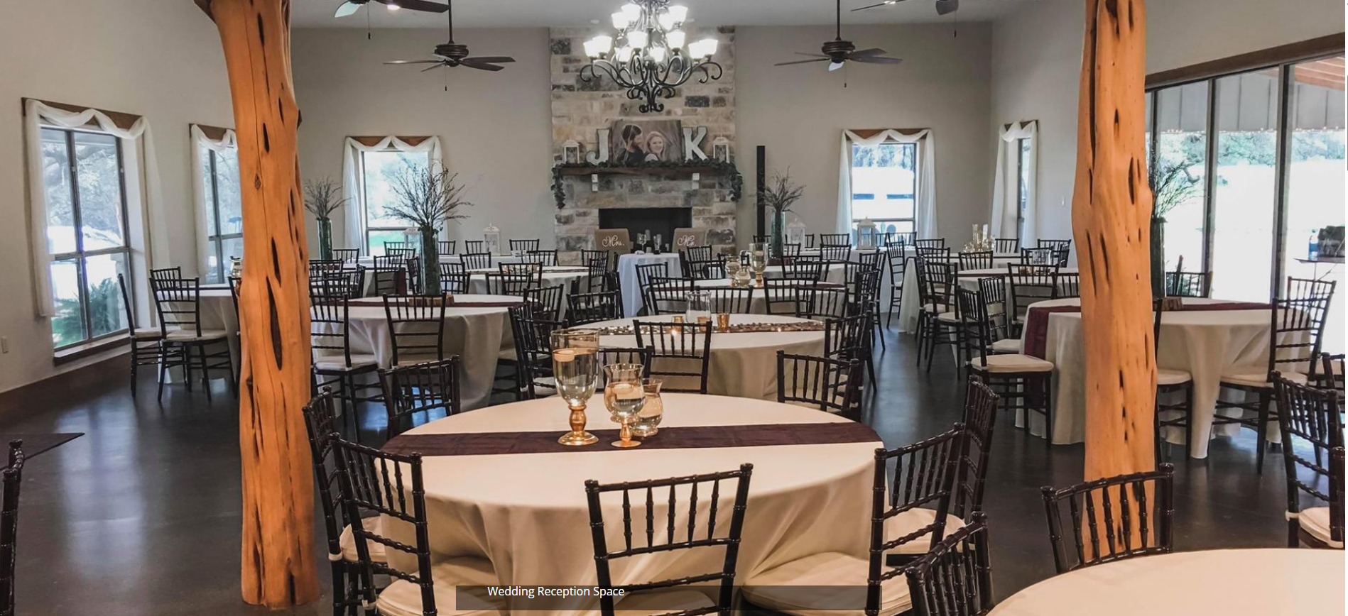 Elegant banquet hall with round tables, black chairs, chandeliers, and wooden beams