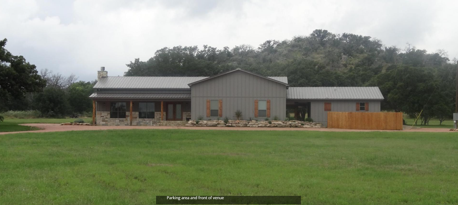 Rural house with a gray roof beside a large green lawn and trees under an overcast sky