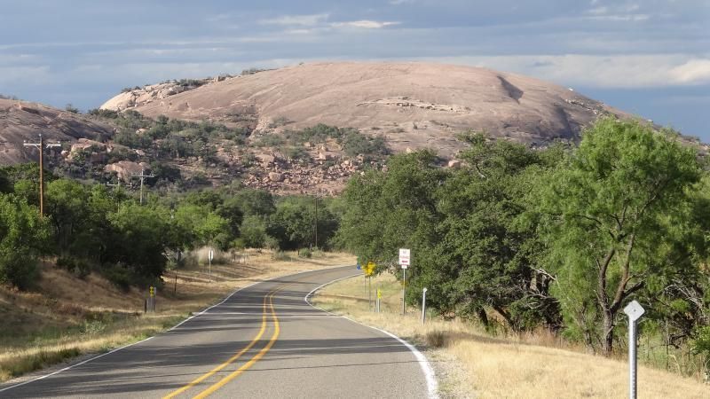 Winding road through green brush toward a large rocky hill under a clear sky