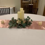 Round table with pink runner, candles, and greenery centerpiece in a banquet room