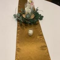 Gold table runner with greenery and a candle centerpiece on a round white table