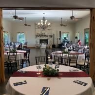 Formal banquet hall with round, set tables, black chairs, chandeliers, and a fireplace at the far wall