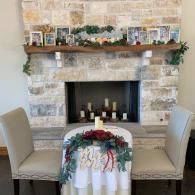 Decorated fireplace mantel with candles and greenery above two beige chairs and a small table centerpiece