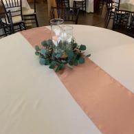 Round table with blush pink runner and greenery centerpiece in a banquet hall