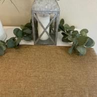 White lantern with candle on a woven mat, flanked by green eucalyptus garlands