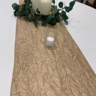 White candle centerpiece with greenery on a beige textured table runner.