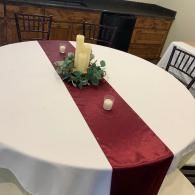 Round banquet table with white cloth, red runner, candle centerpiece, and small votive candle in a dining room
