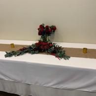 Red floral cross centerpiece on a white-draped table against a plain wall.