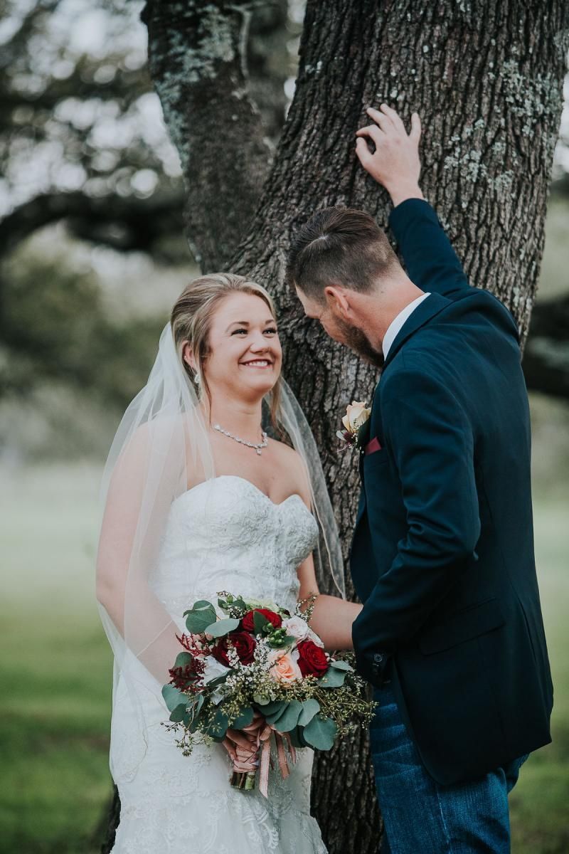 Bride and groom smiling by a tree, bride holding bouquet, outdoors