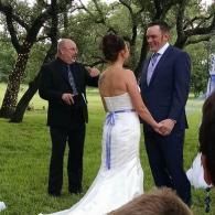 Outdoor wedding ceremony with couple holding hands and officiant standing nearby under trees
