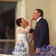 Bride feeds groom cake beside decorated wedding cake indoors