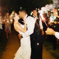 Couple kissing at their wedding while guests hold sparklers at night