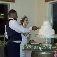 Man in vest and woman in white dress cutting a tiered wedding cake at a reception