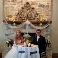 Bride and groom seated at decorated wedding table in front of a stone fireplace