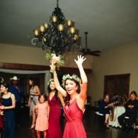 Woman in a red dress raises her arms while holding a bouquet at an indoor celebration