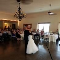 Bride and groom dancing at a wedding reception in a banquet hall with seated guests.