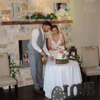 Couple cutting a decorated cake at a wedding reception table in a rustic indoor venue