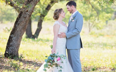 Bride and groom embracing outdoors in a sunlit garden, with a bouquet of pink and white flowers