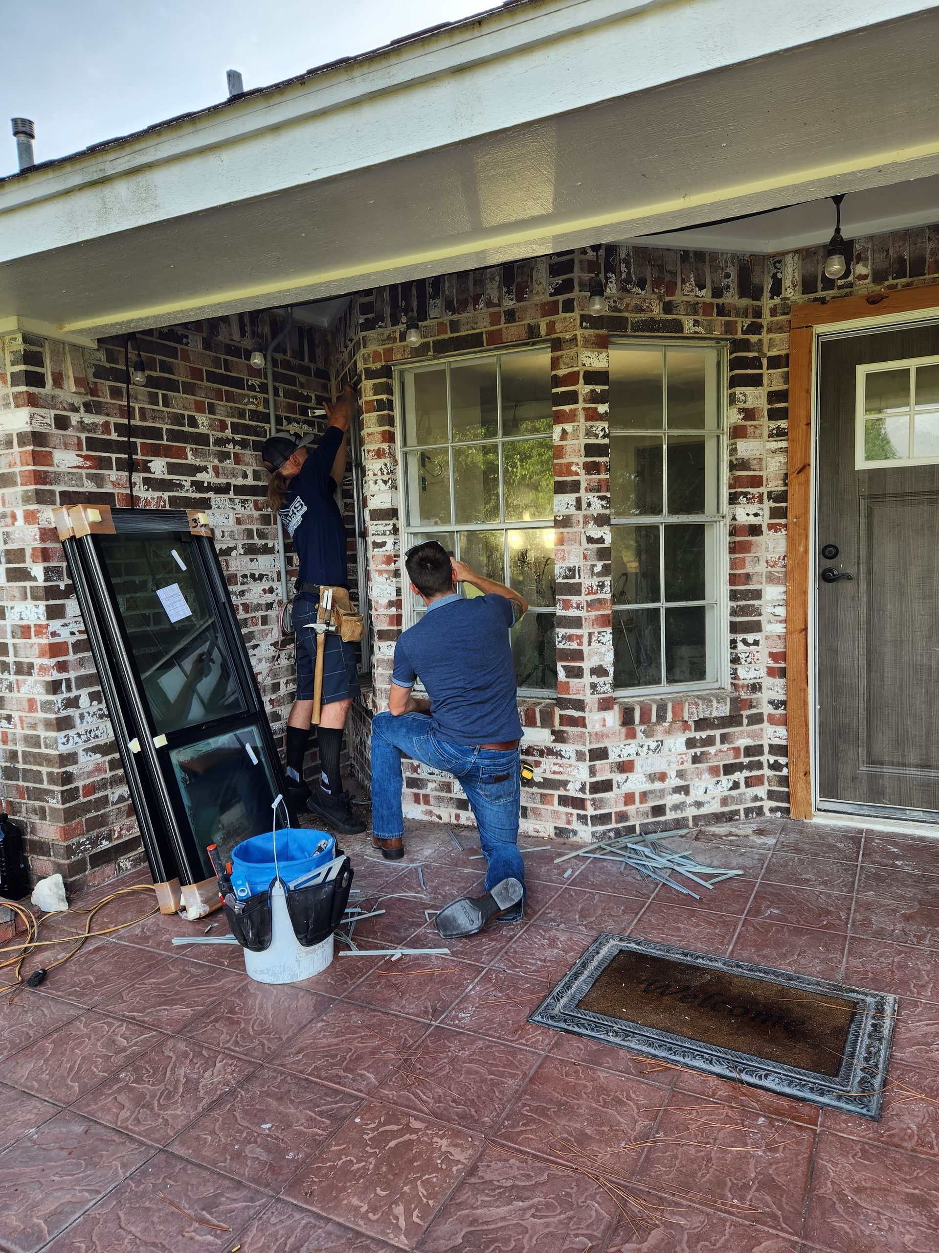 Two men are installing a window on a brick house.