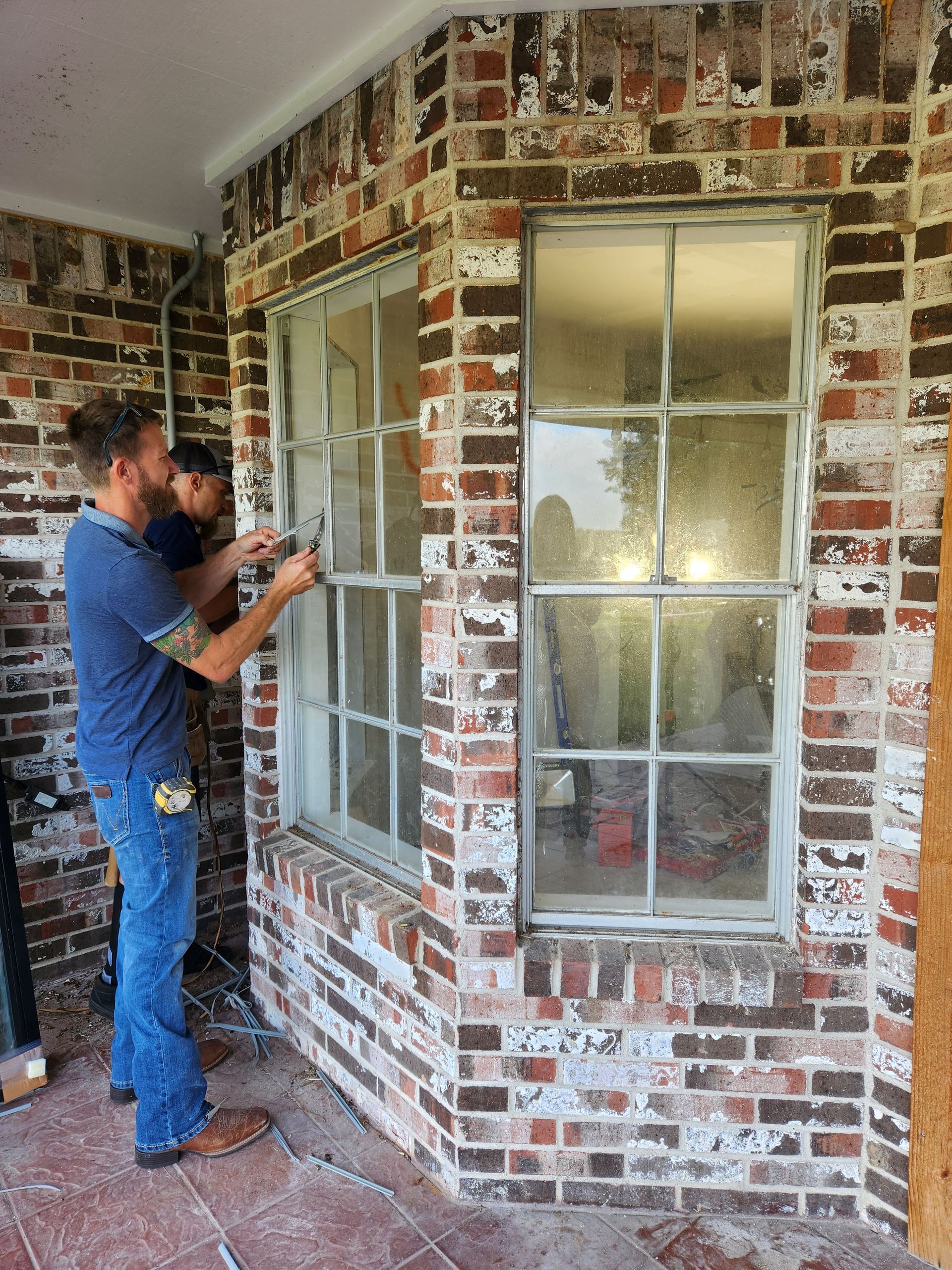 Two men are working on a window on a brick wall
