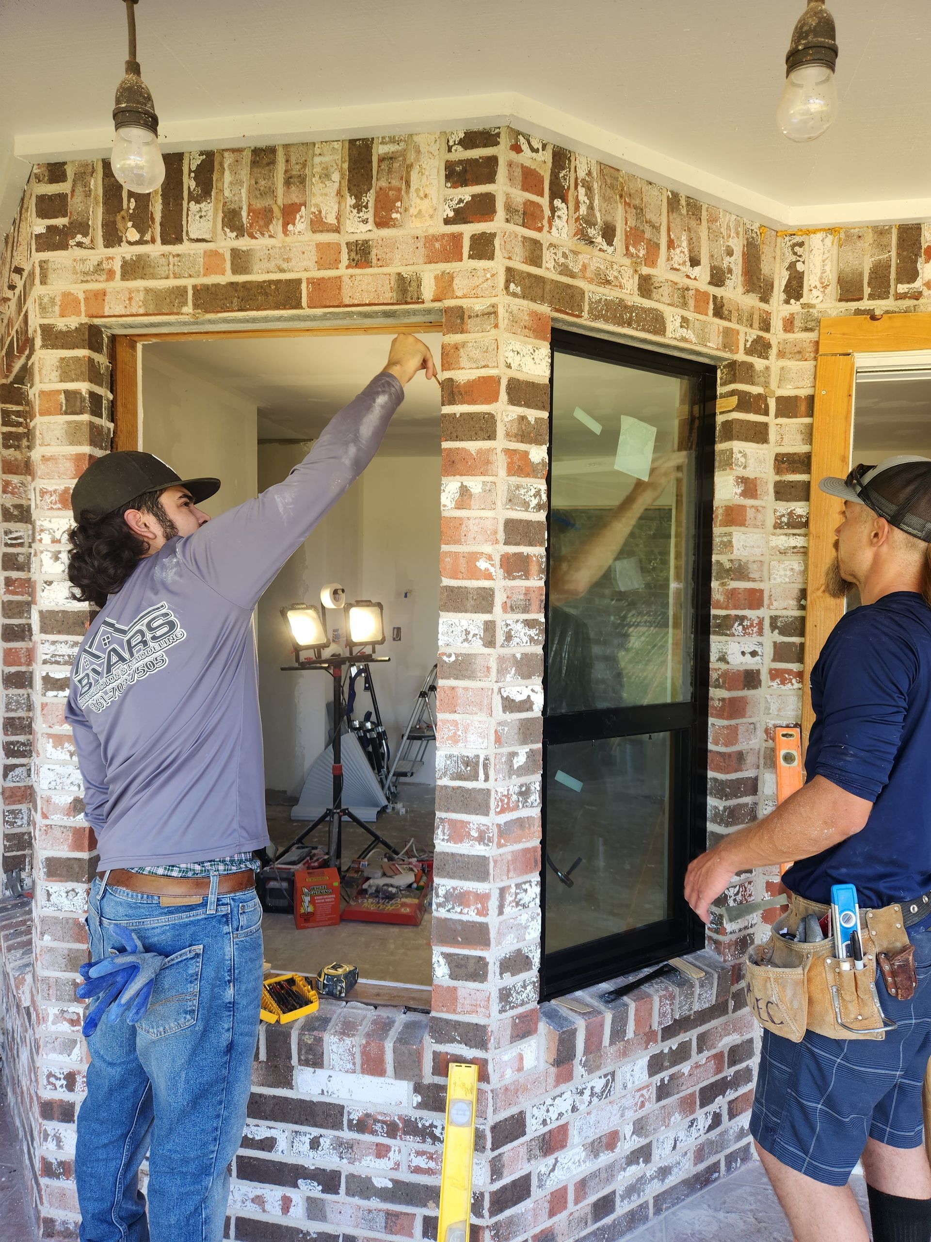 Two men are working on a window in a brick wall.