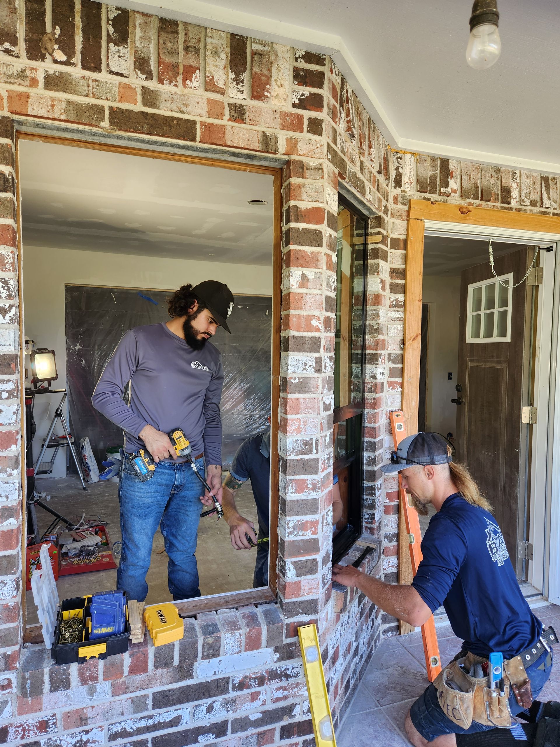 Two men are working on a window in a brick building.