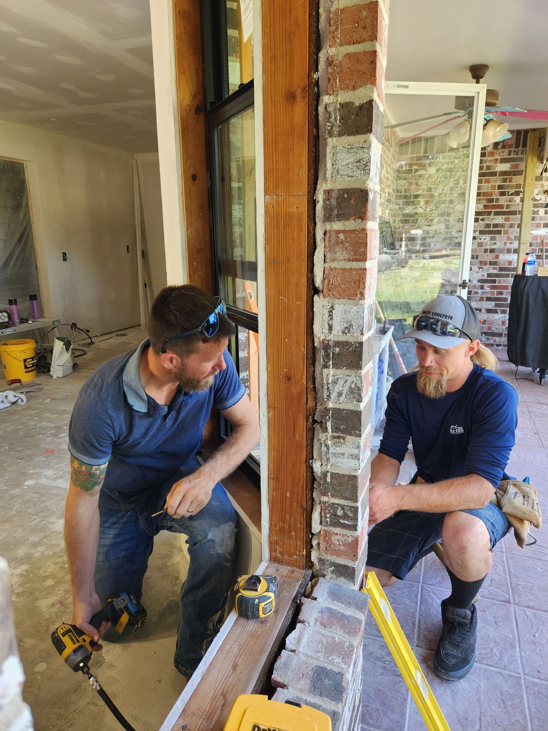 Two men are working on a brick wall in a room.