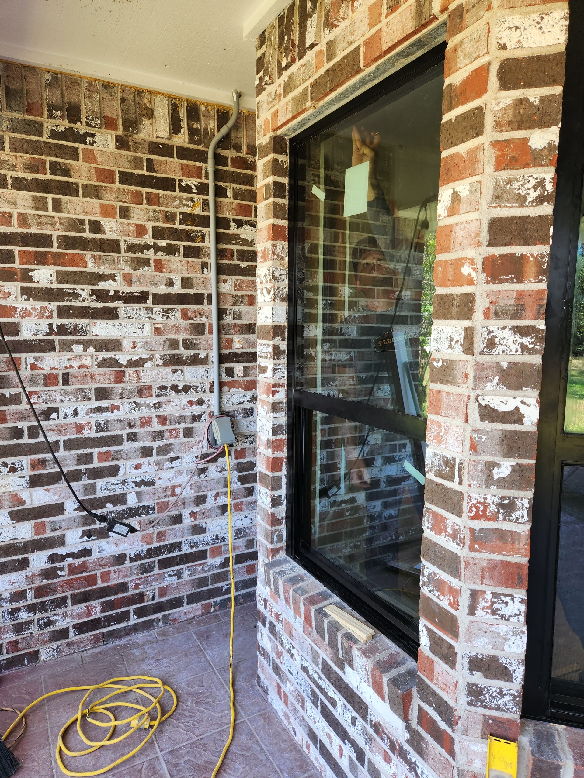 A brick wall with a large window and a yellow power cord.