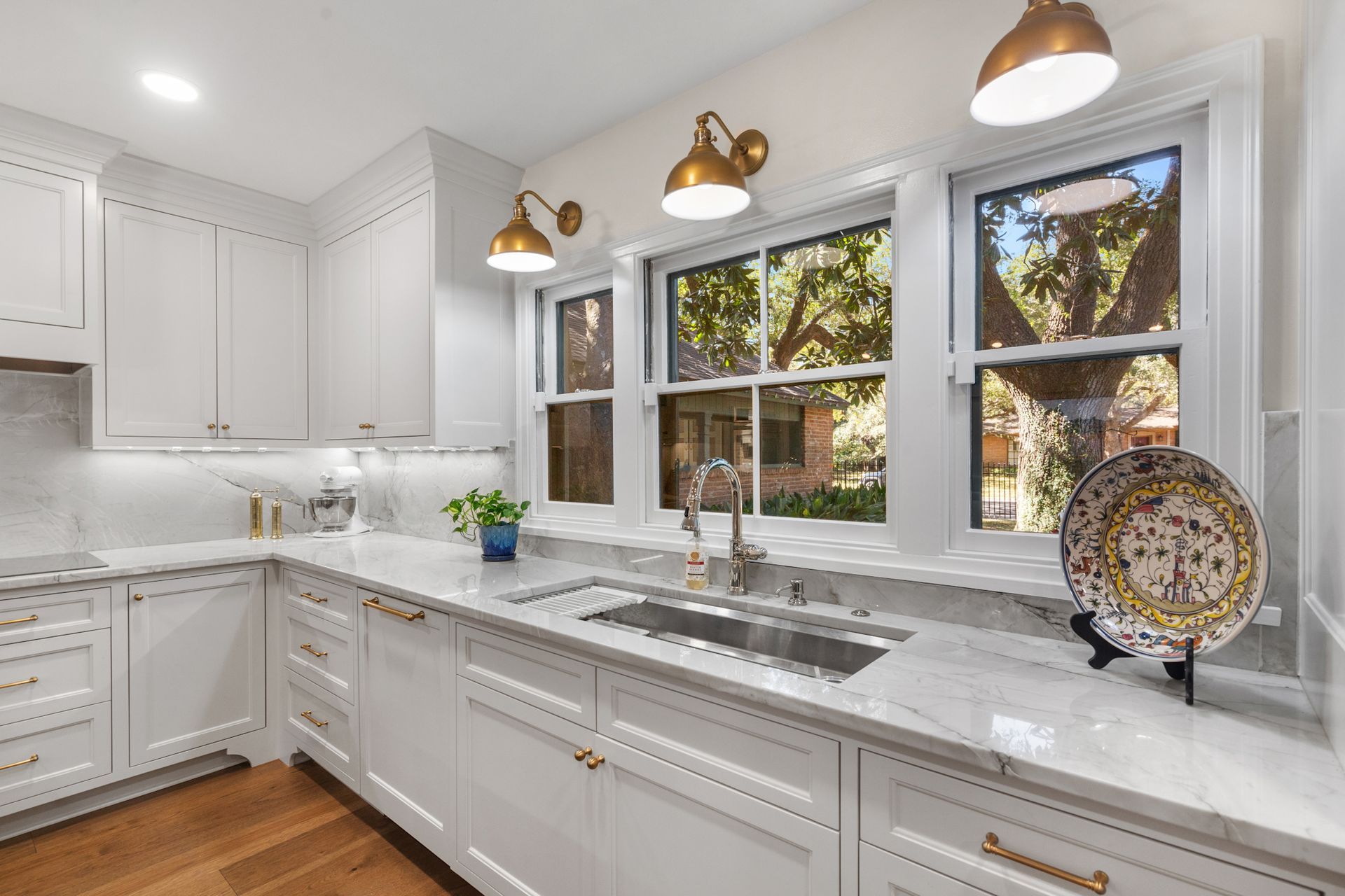 A kitchen with white cabinets , marble counter tops , a sink , and two windows.