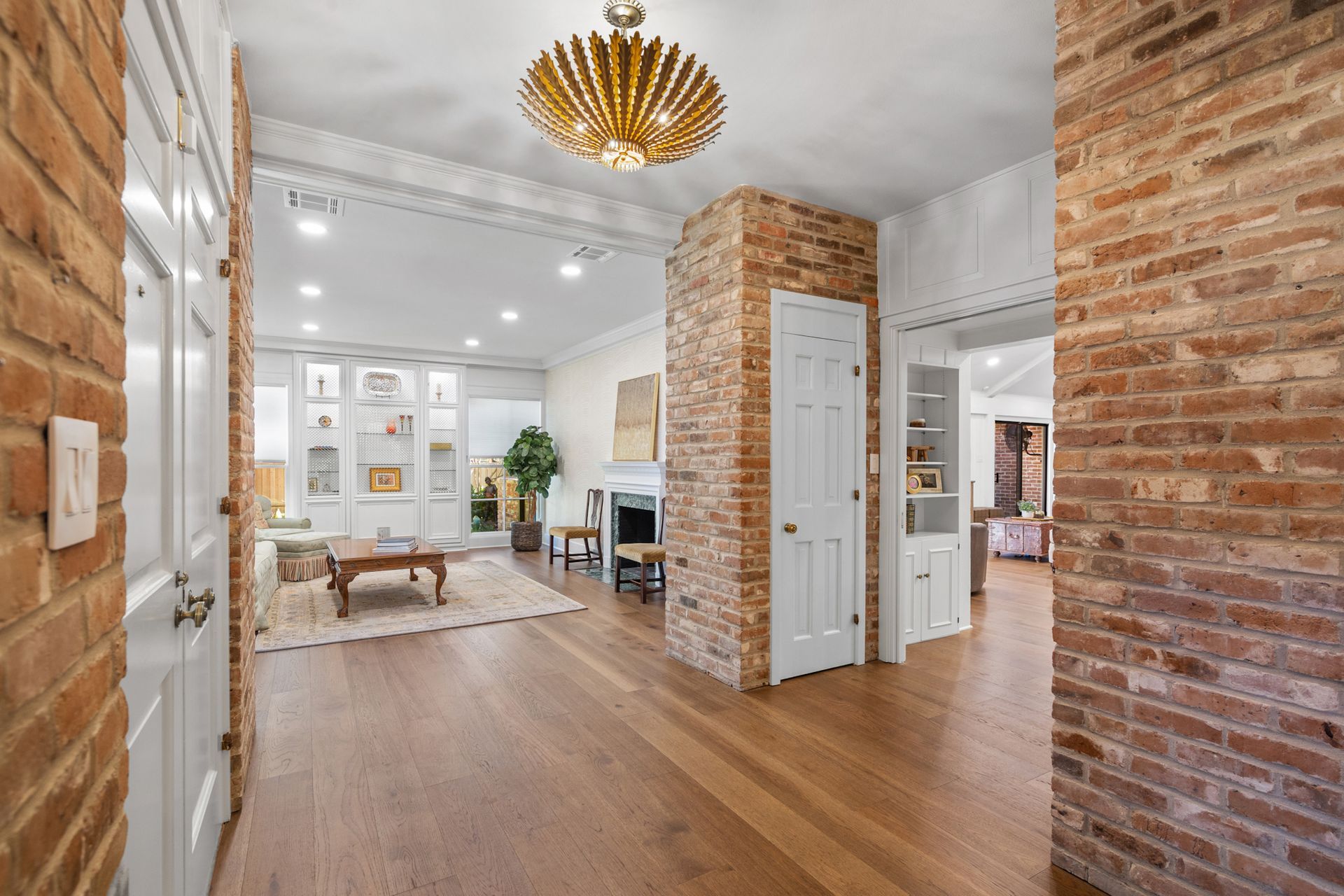 A hallway leading to a living room with hardwood floors and brick walls.