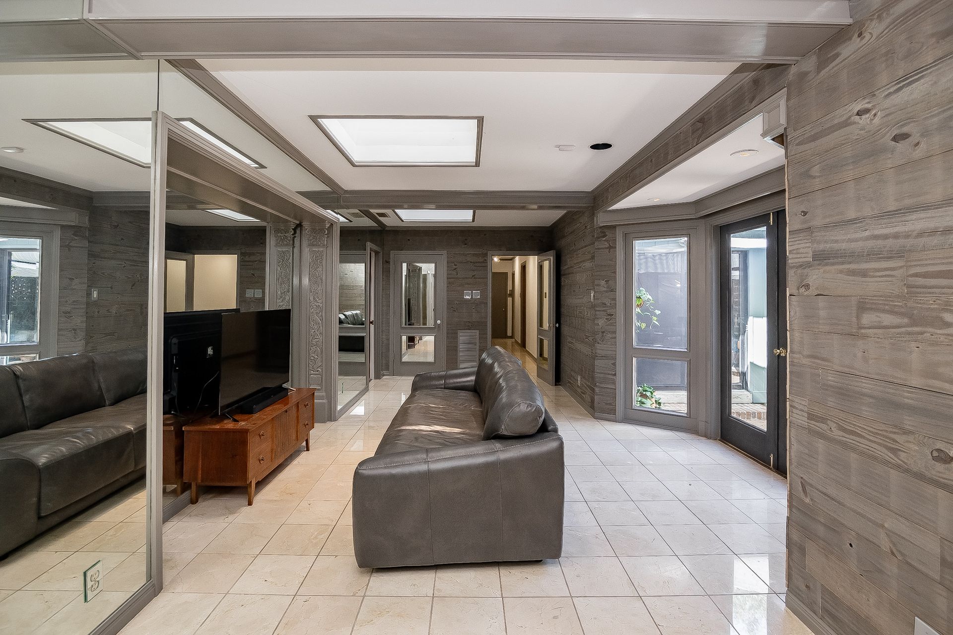 A living room with a couch , television , and mirrors.