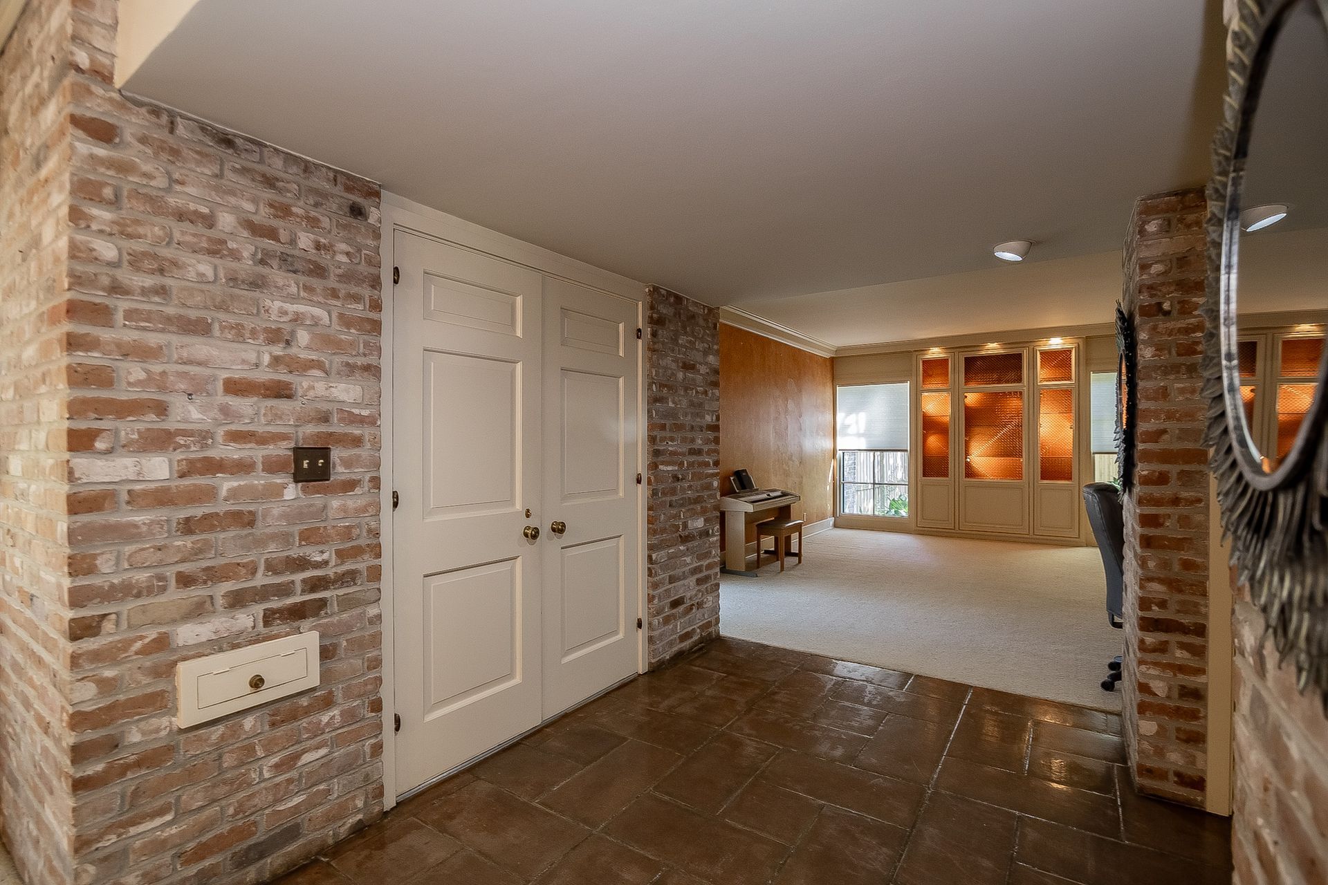 A hallway with a brick wall and white doors leading to a living room.