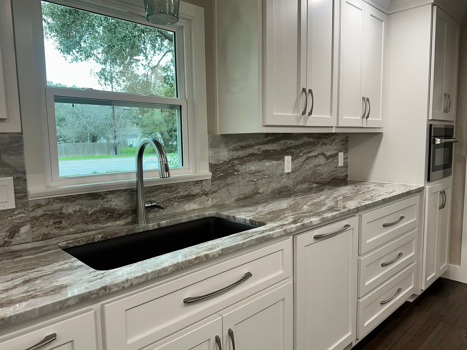 A kitchen with white cabinets , granite counter tops , a sink and a window.