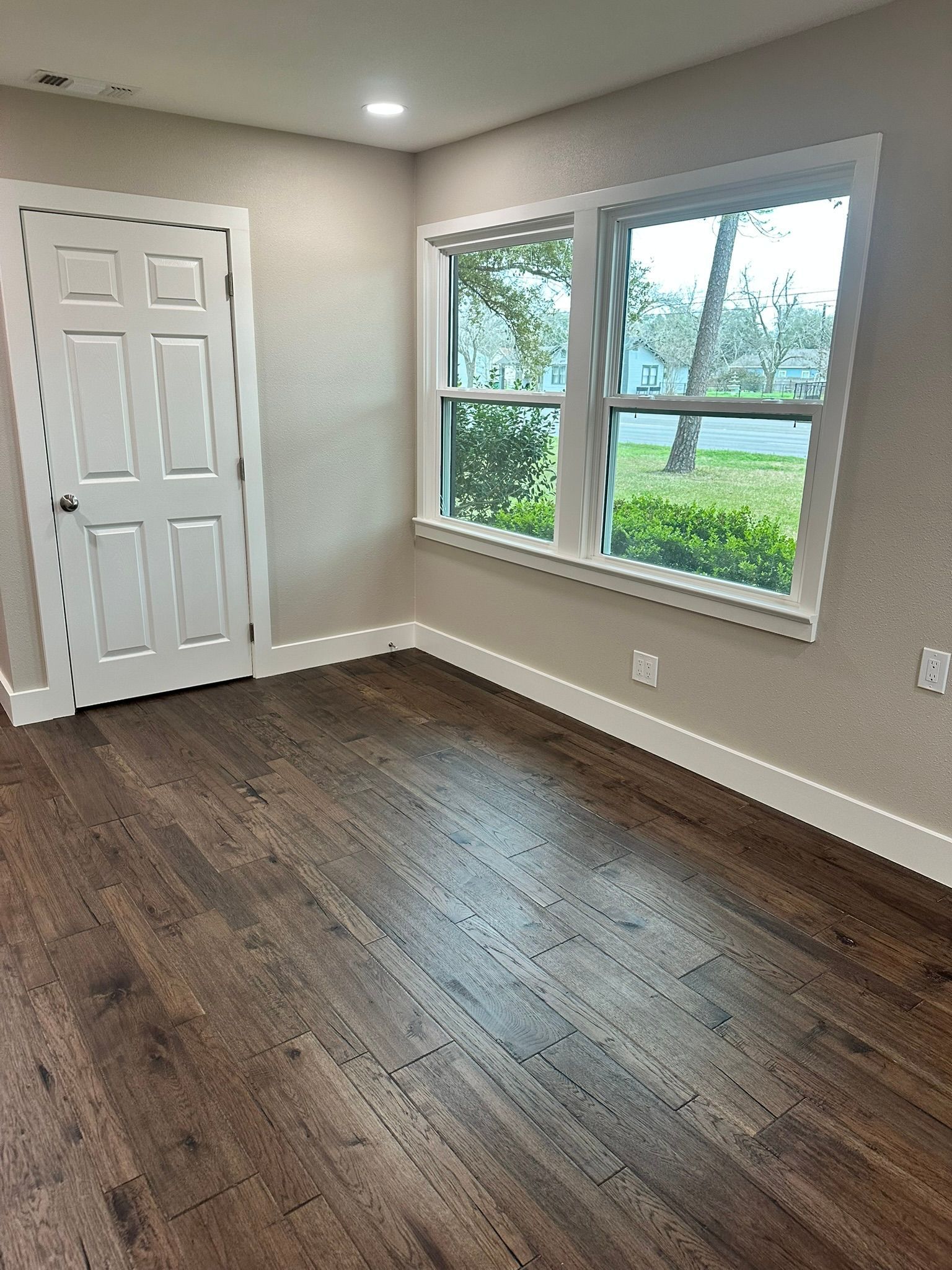 An empty room with hardwood floors and two windows.