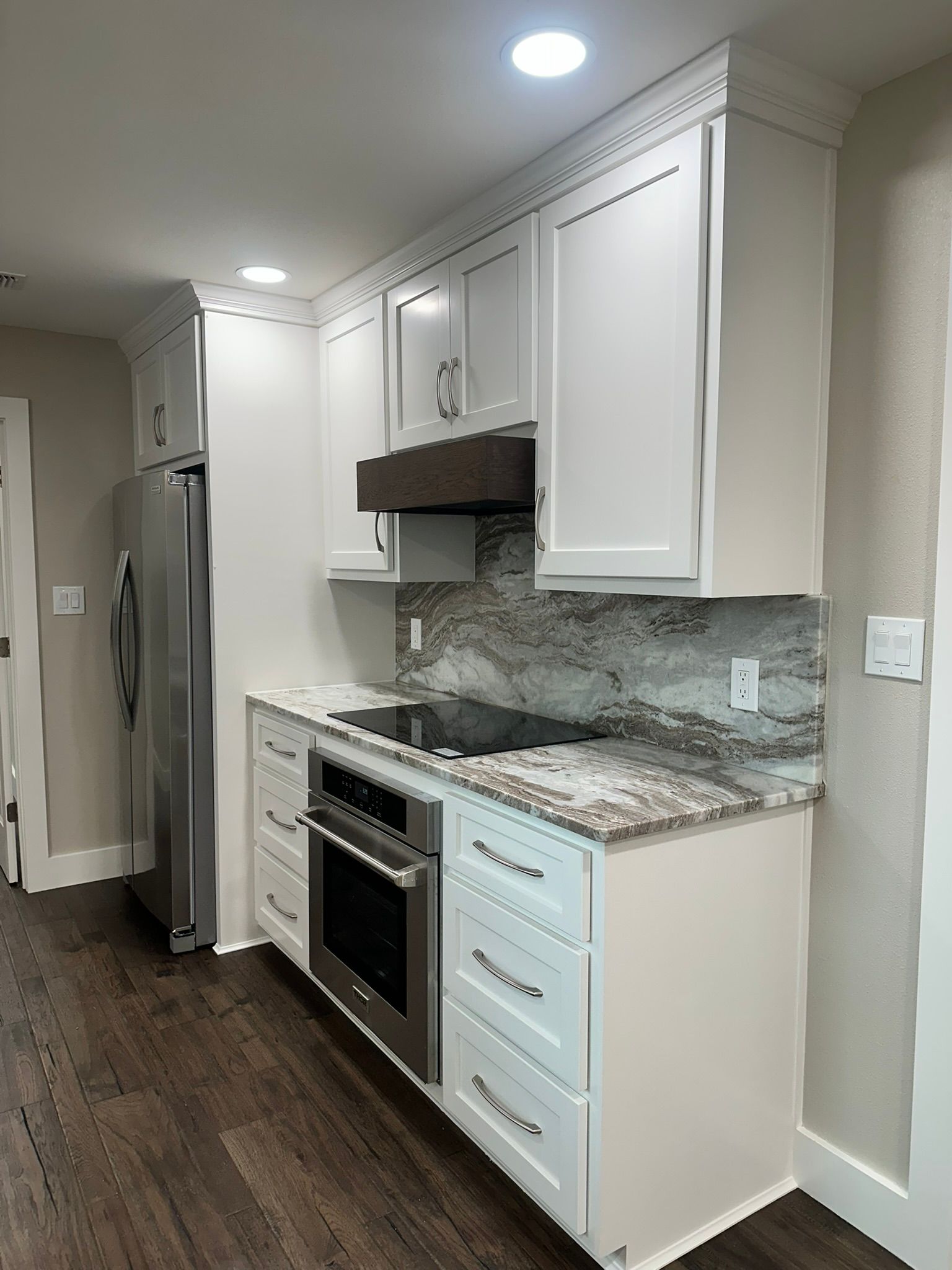 A kitchen with white cabinets , stainless steel appliances , granite counter tops and hardwood floors.