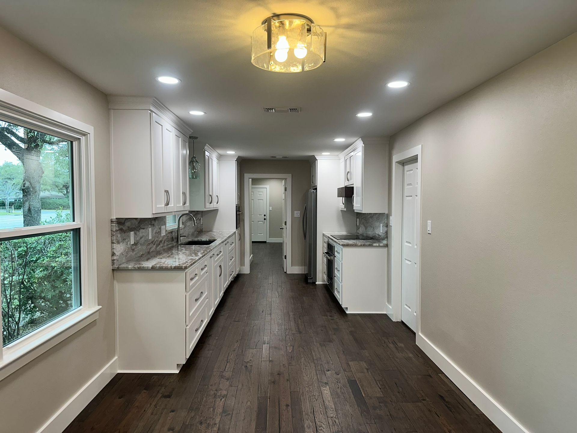 An empty kitchen with white cabinets and hardwood floors
