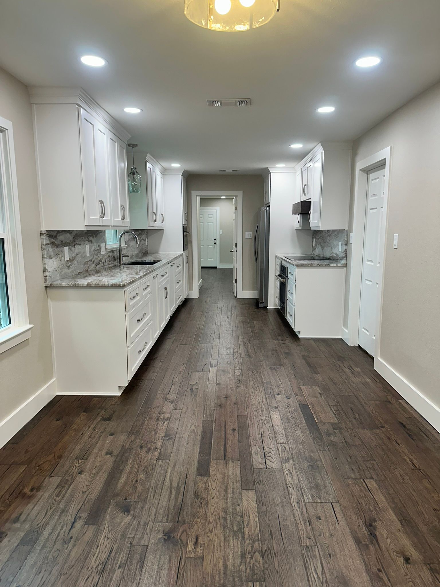 An empty kitchen with hardwood floors and white cabinets.